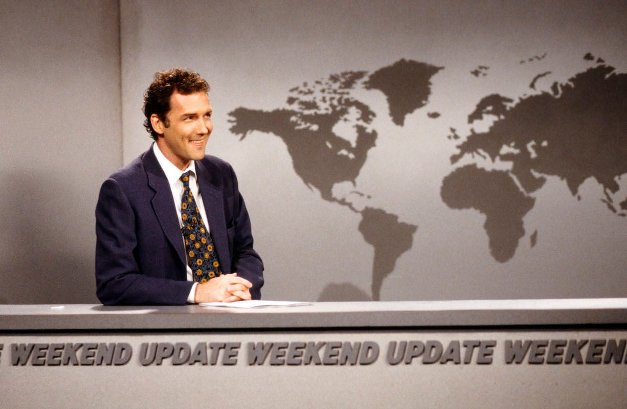 《周六夜现场》:诺姆·麦克唐纳(Norm Macdonald)双手合十坐在周末新闻播报台上