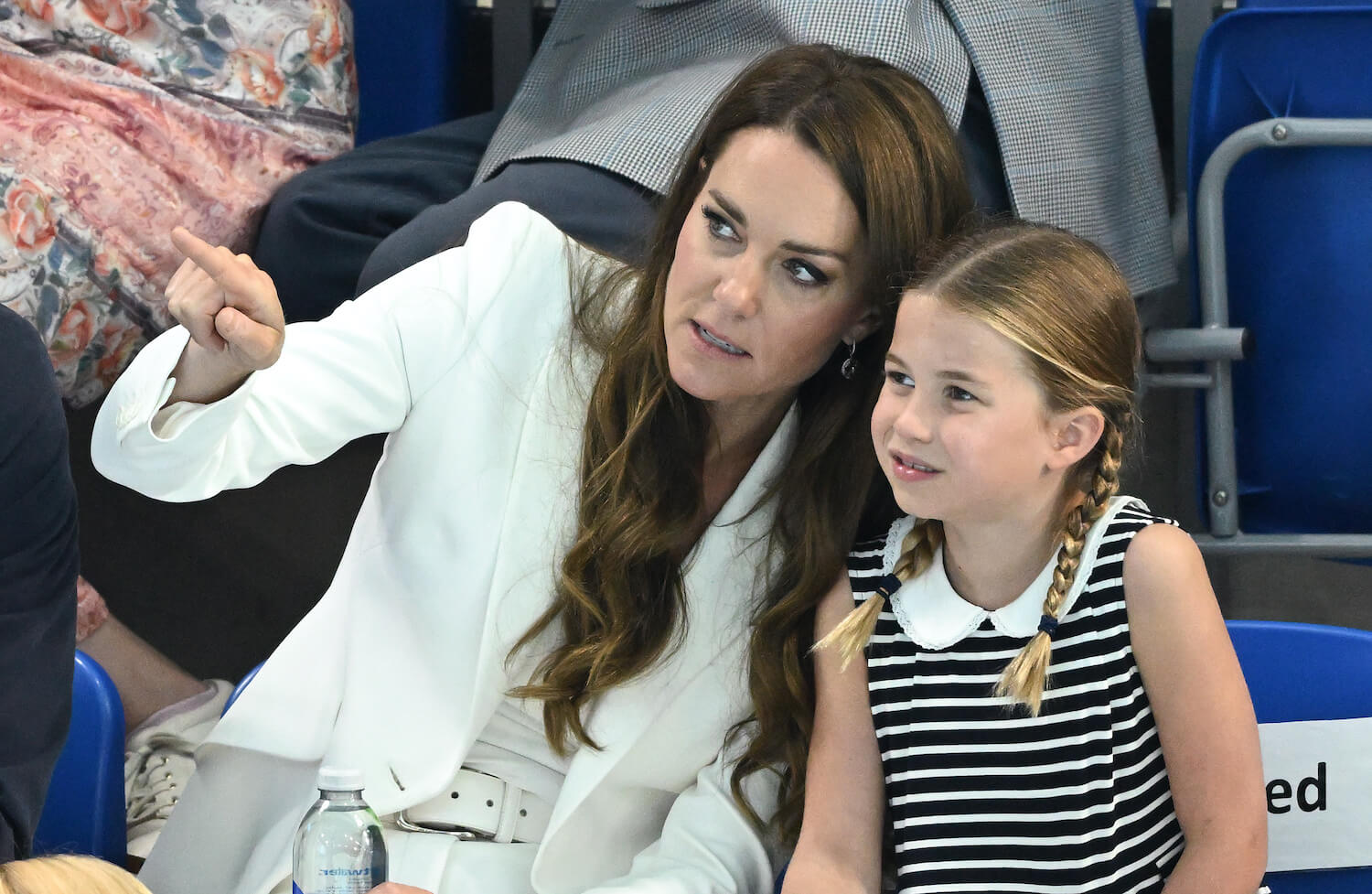 凯特王妃身穿白色外套，用手指着与身穿黑白条纹长裙的女儿夏洛特公主交谈