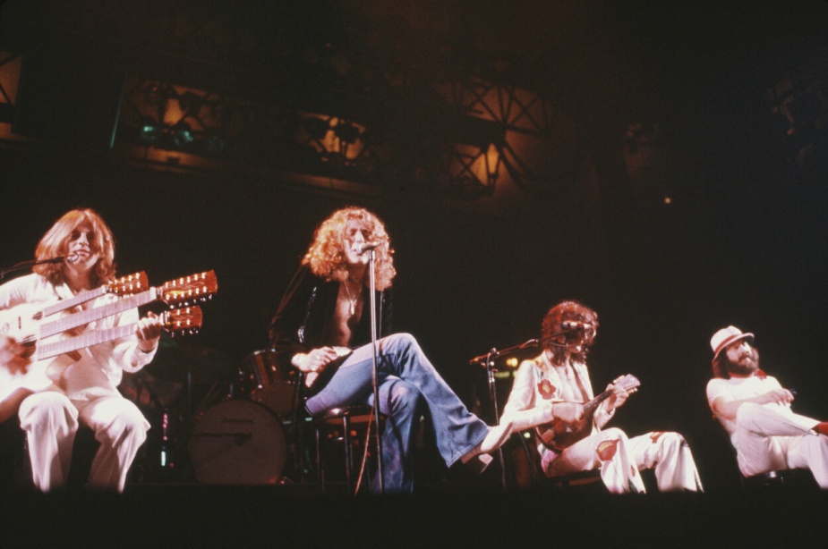 1977年，齐柏林飞艇乐队的成员(左起)约翰·保罗·琼斯、罗伯特·普朗特、吉米·佩奇和约翰·博纳姆坐在舞台前面的椅子上。